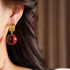 Gros plan de boucles d'oreilles créoles dorées avec perle en résine rouge sur un modèle