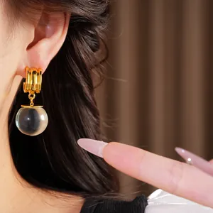 Détail de boucles d'oreilles dorées avec une boule en résine transparente portée