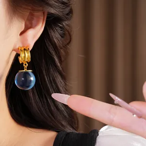 Gros plan de boucles d'oreilles géométriques en or avec une sphère en résine bleue.