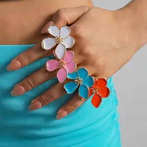 Colorful metal flower rings with enamel detail worn on a model hand