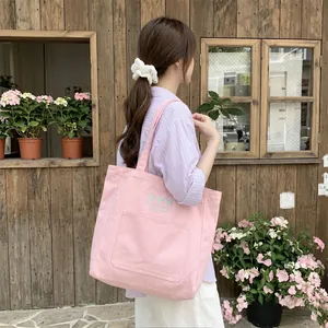 Détail d'un sac cabas en toile rose avec nœud brodé, porté par un mannequin dans un décor naturel
