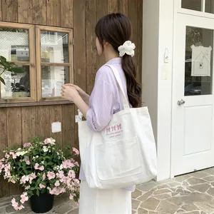 Femme asiatique portant un grand sac cabas blanc en toile brodé d'un nœud rose.