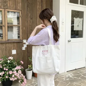 Vue détaillée d'un sac cabas en toile blanche avec broderie nœud rose et texte