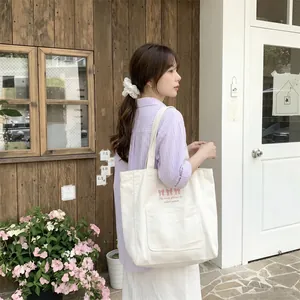 Grand sac cabas en toile blanche avec broderie de nœud rose porté par une femme