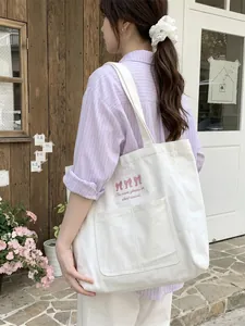 Casual white canvas tote bag featuring pink bow embroidery and a front storage pocket