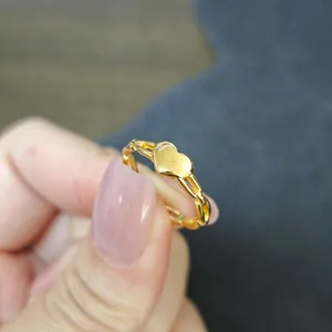 Vista dettagliata di un anello a cuore in acciaio al titanio dorato tenuto da una mano.