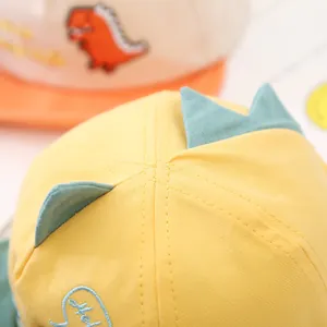 Detailed close-up view of yellow cotton baby baseball cap with cute blue dinosaur spikes