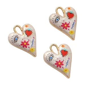 Detailed view of white enamel heart pendants with hand-painted floral and eye motifs