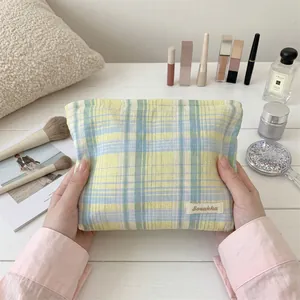 Close-up of a soft checkered yellow and blue cosmetic bag held by hands on a desk.