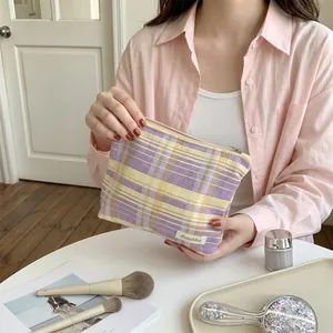 Close-up of a yellow and purple checkered makeup bag held by a person in a lifestyle setting