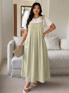 Full-length view of a sage green plus-size pinafore dress over a white t-shirt