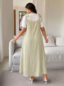 Back view of a plus size solid sage green pinafore dress with adjustable bow straps