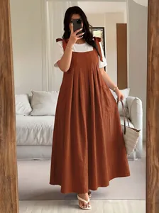 Plus size burnt orange pinafore dress styled with a white t-shirt in a home setting