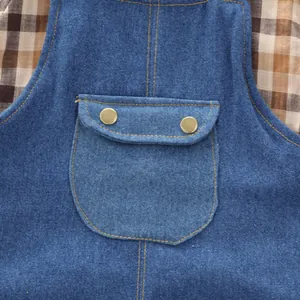 Close-up of children's denim overalls pocket with brass buttons and plaid shirt background.