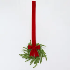 Detailed view of the Norfolk pine Christmas wreath with a long red velvet bow ribbon.