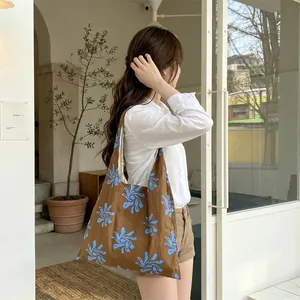 Side view of a brown canvas tote bag with a blue floral print carried by a model