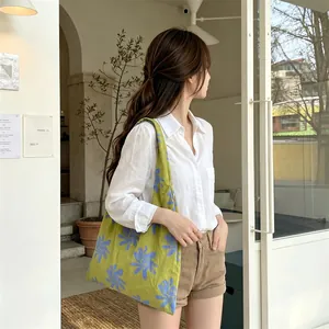Lifestyle detail shot of a woman carrying a green floral canvas tote bag in a cafe.