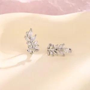 Macro view of shimmering zircon wheat stalk ear clips on a soft cream background.
