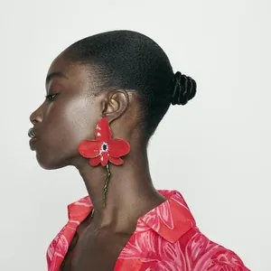 Professional detail view of an exaggerated red orchid flower earring on a model.