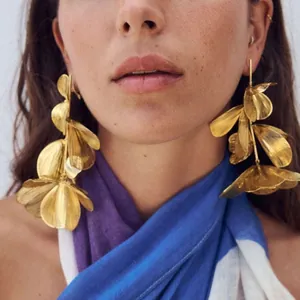 Detailed view of luxury golden oversized 3D floral statement drop earrings worn by model