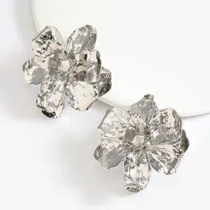 Close-up detail of oversized silver 3D flower earrings with hammered metallic texture