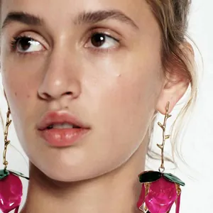 Close-up of model wearing vibrant pink 3D flower drop earrings with golden stems