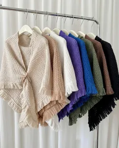 Detailed view of colorful knitted triangular shawls with fringe hanging on a rack.