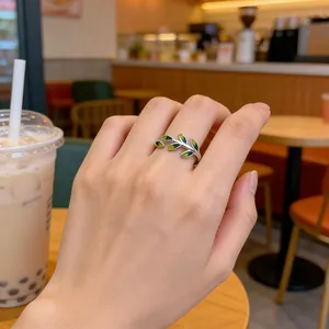 Elegant 925 silver leaf branch ring with green enamel detail worn on hand in a cafe