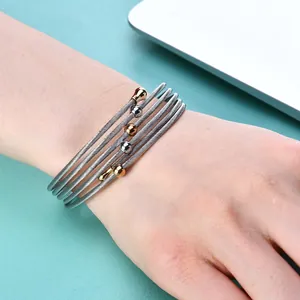 Détail d'un bracelet câble multicouche en acier inoxydable avec perles dorées et argentées.