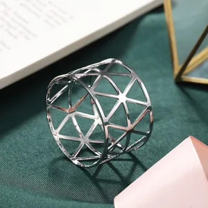 Detailed view of a silver hollow geometric metal napkin ring on green textured fabric backdrop