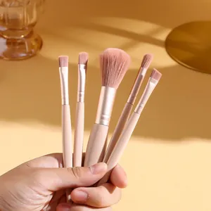 Close-up of a hand holding five mini portable makeup brushes in soft pink and beige tones