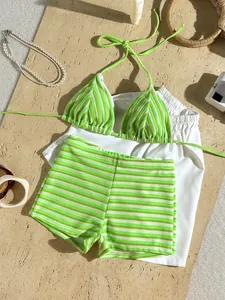 Flat lay of green striped terry cloth bikini set and white shorts on sand background