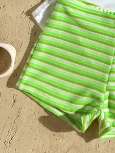 Detailed view of lime green and white striped terry cloth bikini shorts on a sandy stone surface