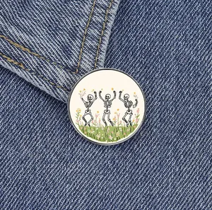 Retro round enamel pin featuring dancing skeletons in a flower field on denim jacket.
