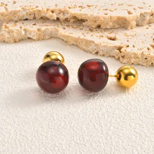 Macro view of minimalist cherry-inspired earrings featuring dark red and gold spheres