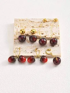 Detailed view of various red cherry fruit earrings on a textured travertine stone block