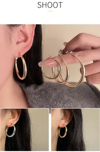 Vue détaillée de trois tailles de créoles dorées minimalistes sur les doigts et l'oreille.