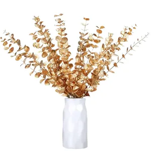 Golden artificial eucalyptus stems in a white vase for Christmas and wedding decor.