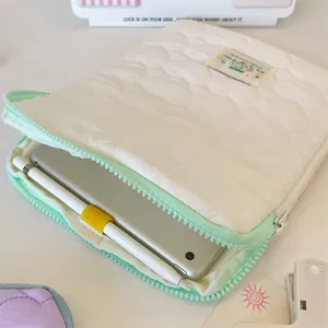 Close-up of a soft quilted iPad sleeve with a mint green zipper and a tablet inside.