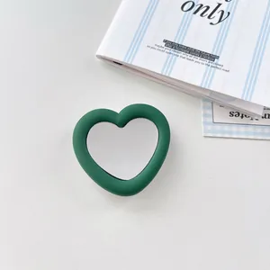 Detail shot of a dark green heart-shaped silicone phone grip with integrated vanity mirror.