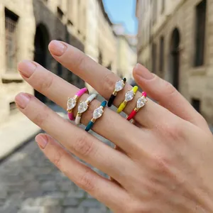 Close-up of a hand wearing various colorful enamel teardrop rings with sparkling zircons