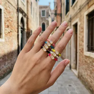 Detailed view of multiple colorful enamel water drop rings on hand in a street setting