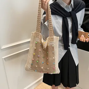 Detail view of a beige crochet tote bag with colorful pearl accents worn on shoulder.