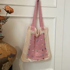 Hand-knitted hollow-out shoulder bag with colorful beads decoration hanging on a white door