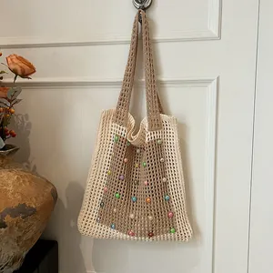 Casual hollow-out knitted tote bag with colorful bead accents hanging on a white door.