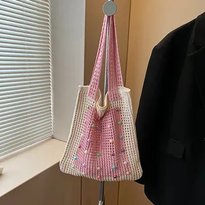 Handmade pink and cream knit tote bag with colorful pearls hanging in a modern room