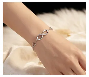 Silver infinity and heart charm bracelet displayed on wrist with fuzzy backdrop