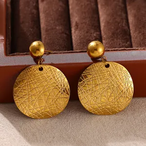Close-up of gold stainless steel circular earrings with textured cross-hatch design.