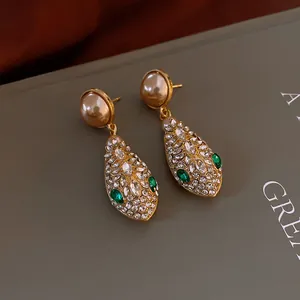 Close-up of vintage gold earrings with pearl studs and green crystal snakehead drops