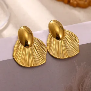 Close-up of chunky gold-toned stainless steel earrings with ribbed scallop detail